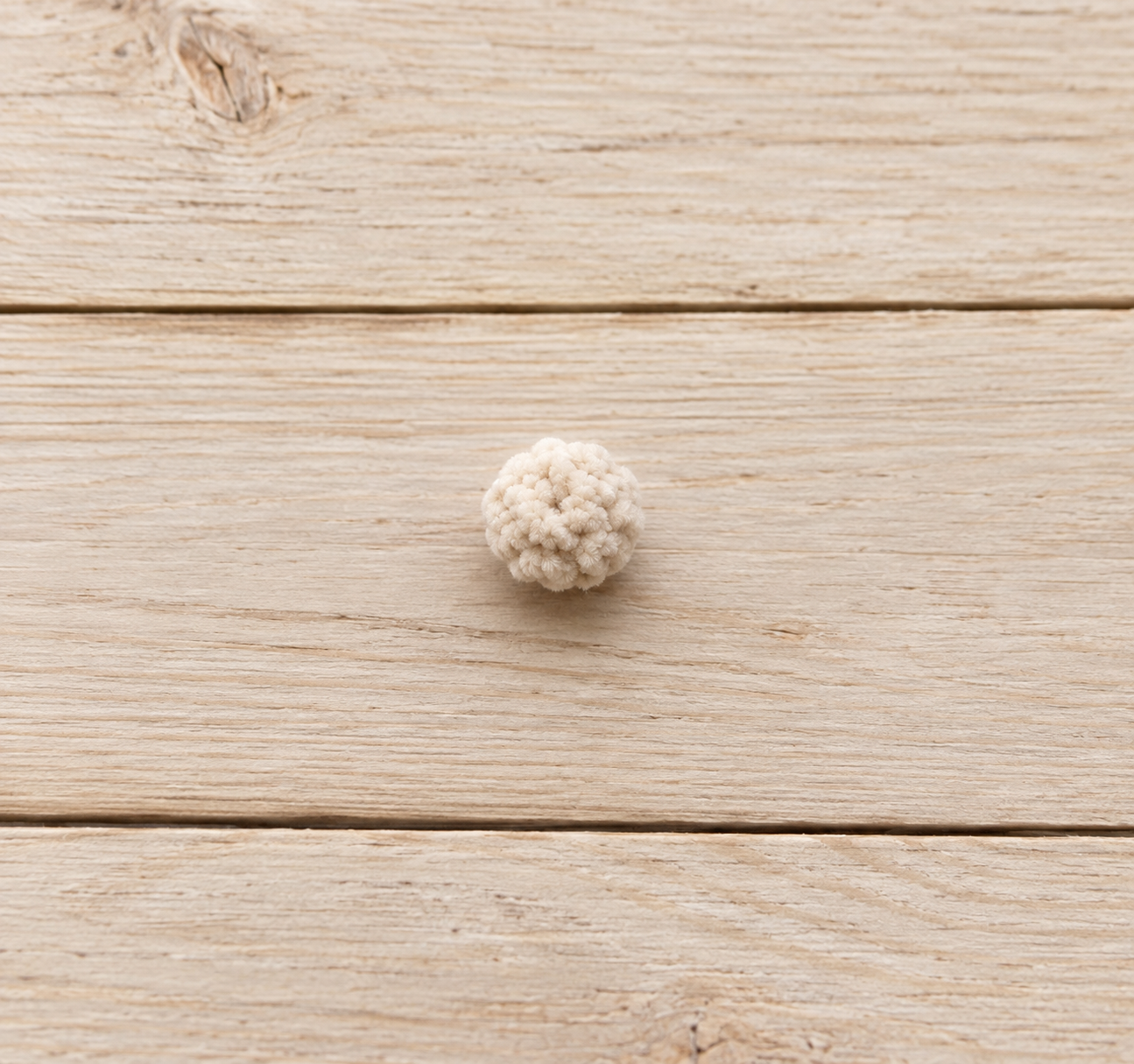 Small cream crochet bunny tail on a wooden surface