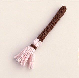 Miniature crochet broom with a brown handle and pale pink yarn bristles