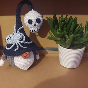 Black hat Halloween crochet gnome next to green houseplant