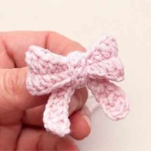 Small pale pink crochet bow with ribbon tails held in a hand