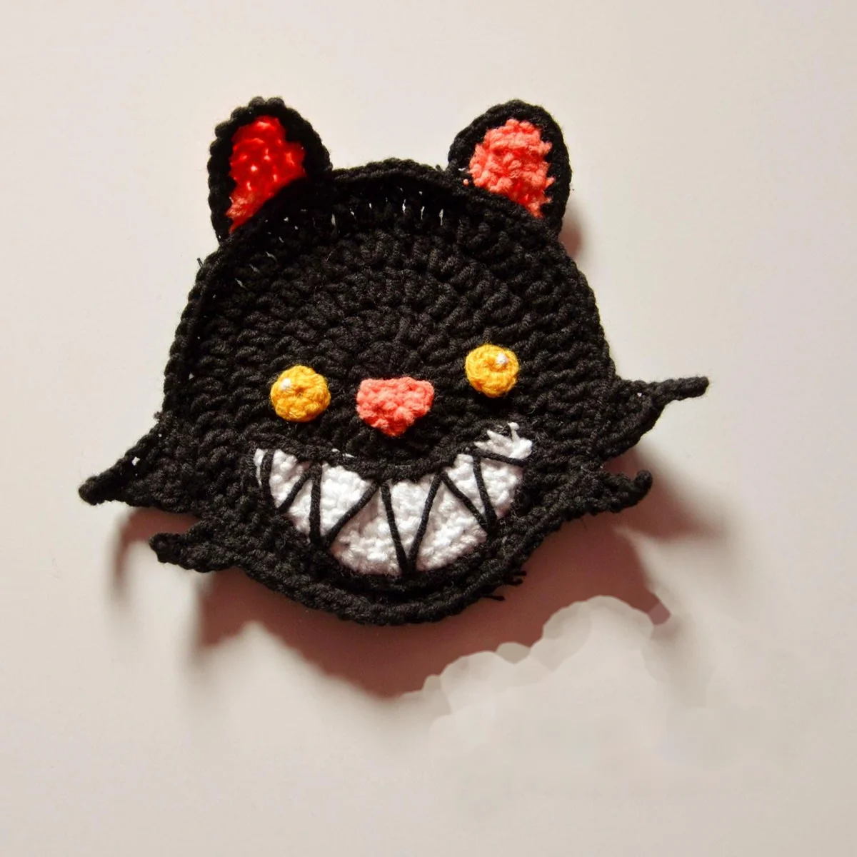 Black Cat crochet coaster with yellow eyes, pink ears and a white grin