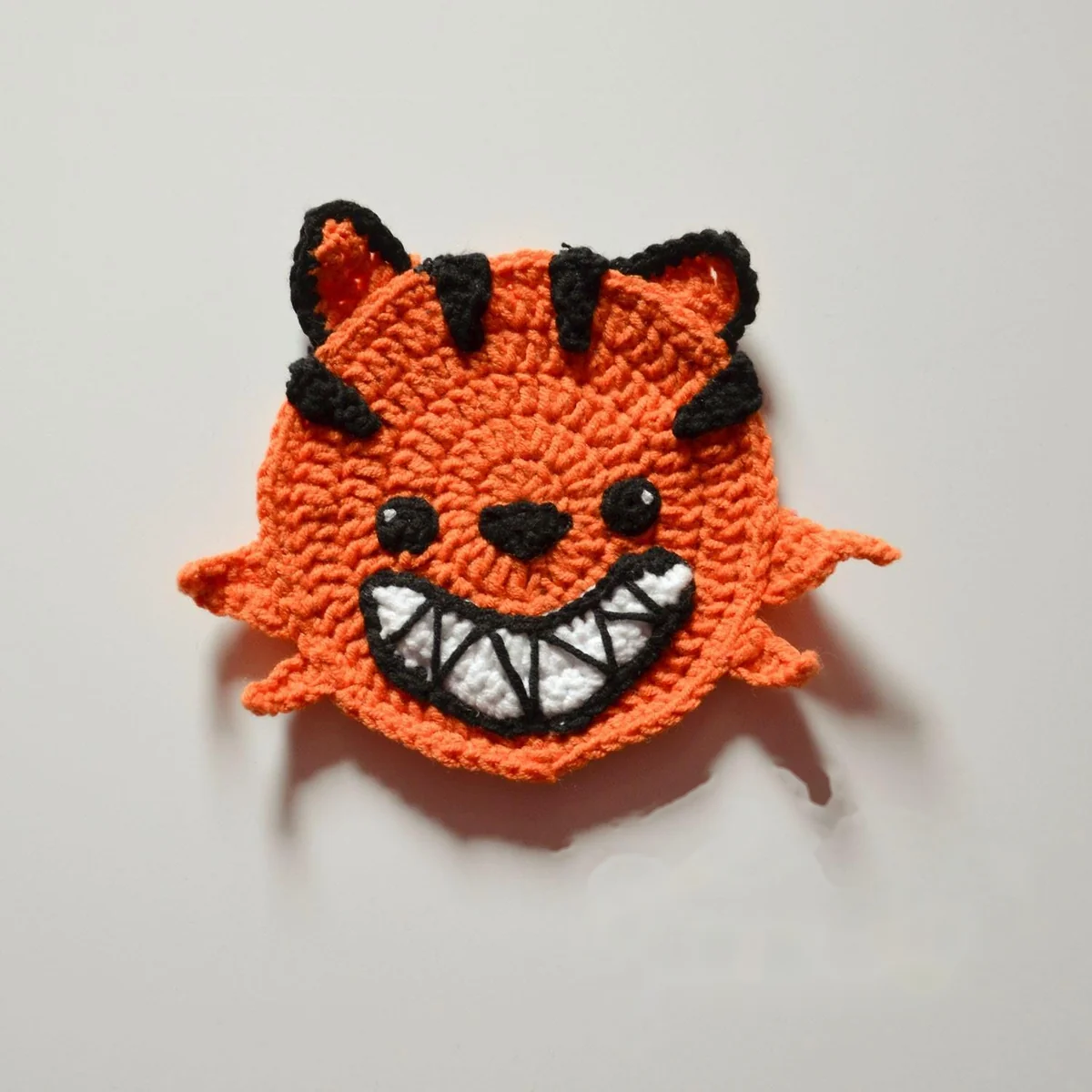 Orange Pumpkin Cat crochet coaster with black stripes and a toothy smile