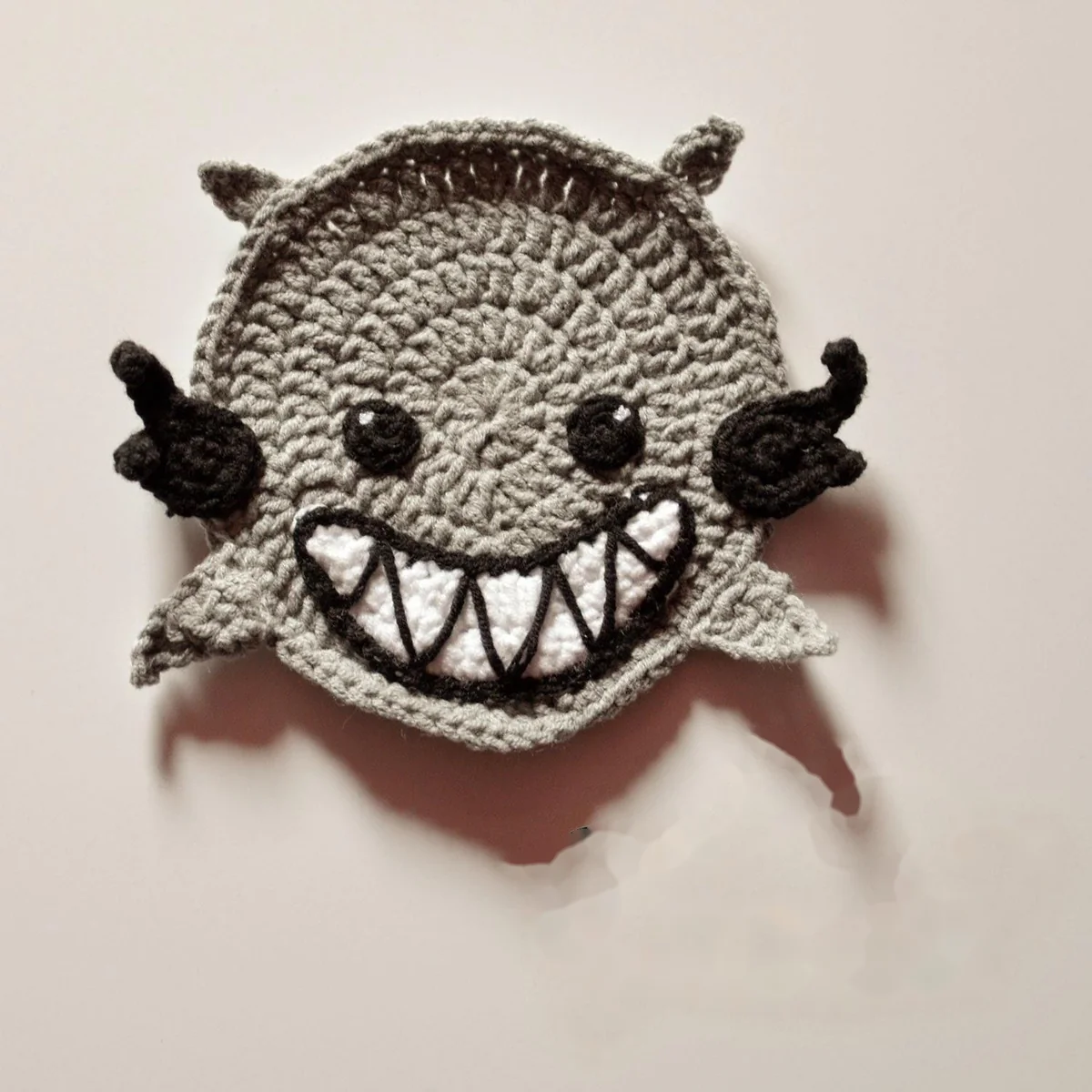 Grey Spirit crochet coaster with black wings and a toothy smile