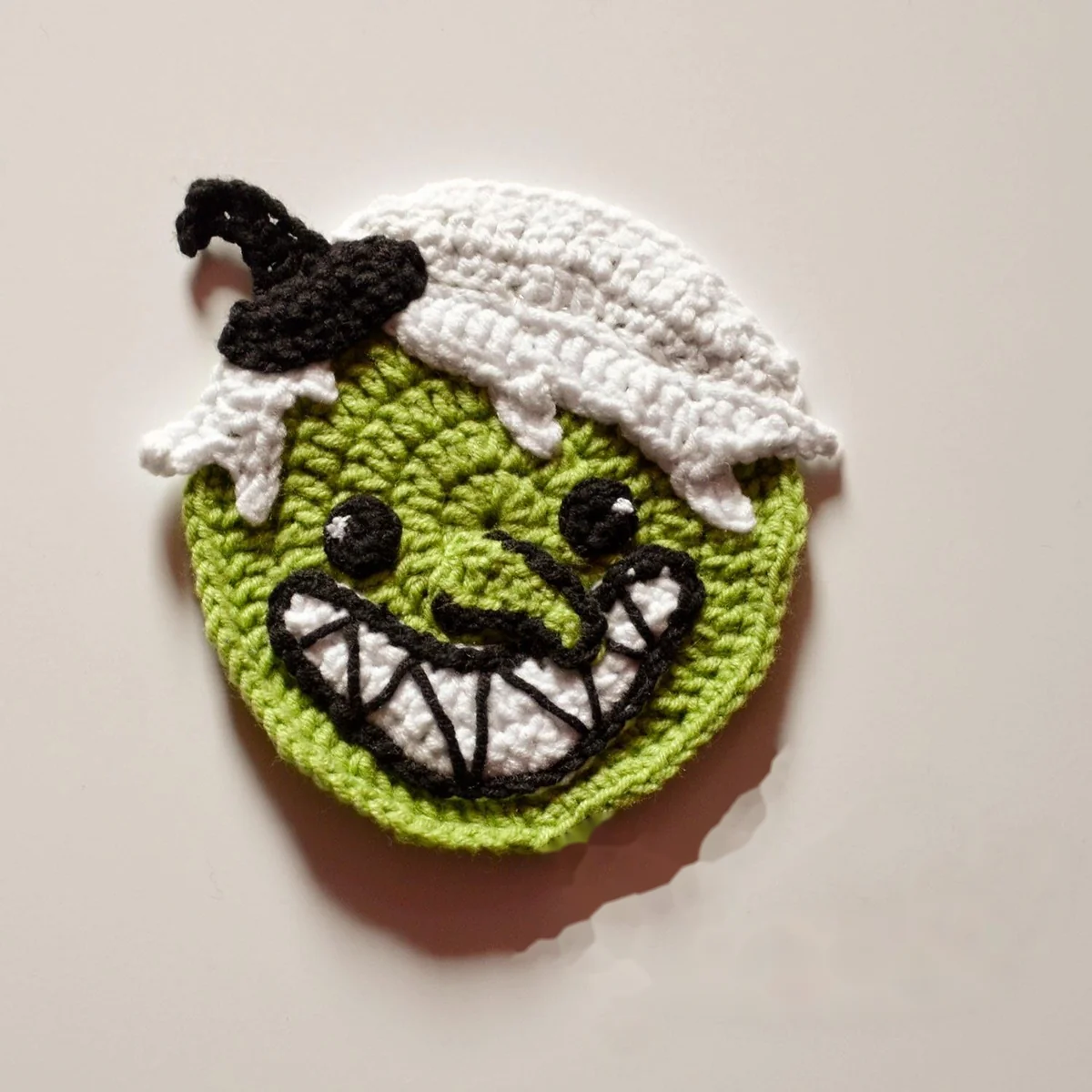 Green Wicked Witch crochet coaster with white hair and a small black hat